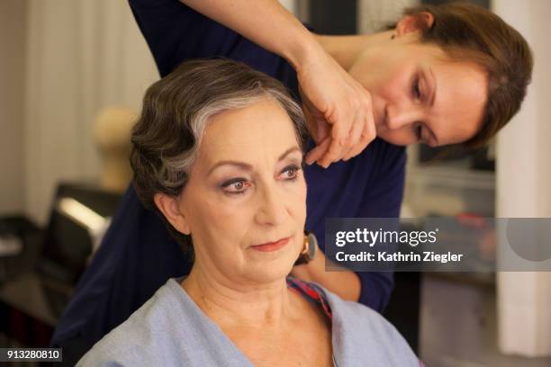 beautiful senior woman having her hair and makeup done by makeup artist before stage performance - backstage hairdresser stockfoto's en -beelden