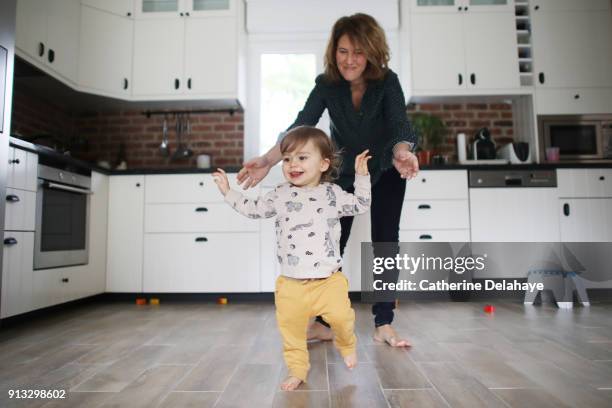 first steps of a 1 year old baby boy in the kitchen - primeiros passos imagens e fotografias de stock