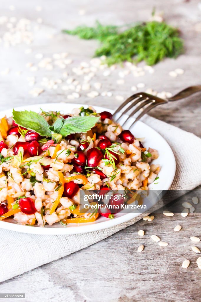 Warm salad with barley, carrot, onion, pomegranate seeds and fresh mint in a plate on a wooden table, selective focus