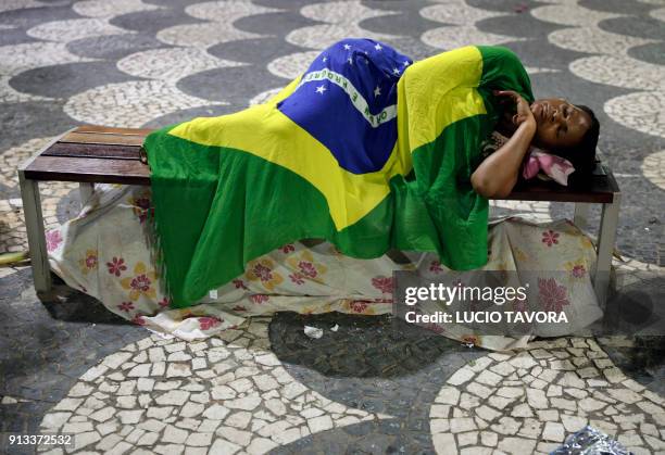 Yemanja faithful covered with a Brazilian national flag, sleeps on a bench beside the beach, before the start Yemanja day celebrations, at Rio...