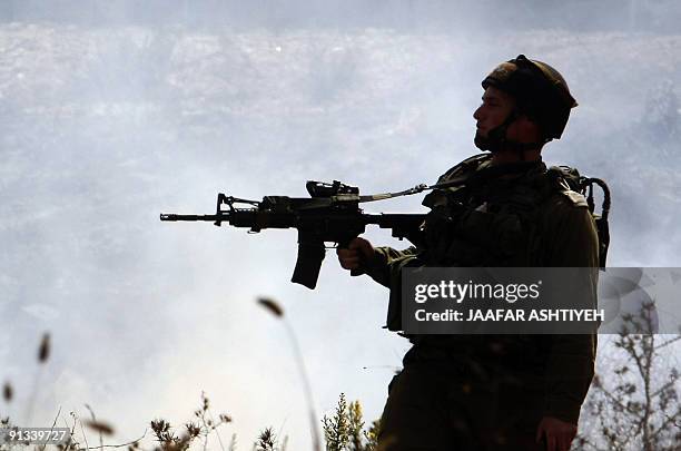 An Israeli soldier points his weapon as Palestinians demonstrating against the closure of a road that leads to the West Bank village of Qarut, near...