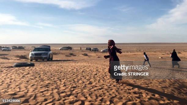 Displaced Libyan woman from the western city of Tawergha walks through the sand, as cars are seen waiting to enter the city, which lies about 250...