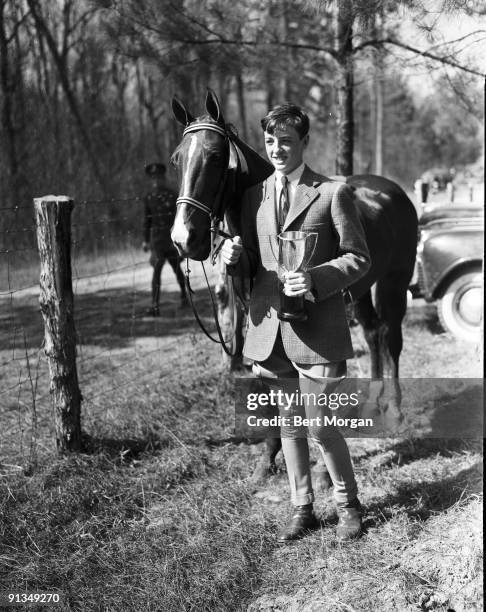 William F Buckley Jr of Horsemanship Class holding onto the reins of his horse Pickles with one hand and onto a trophy with the other, at the Camden...
