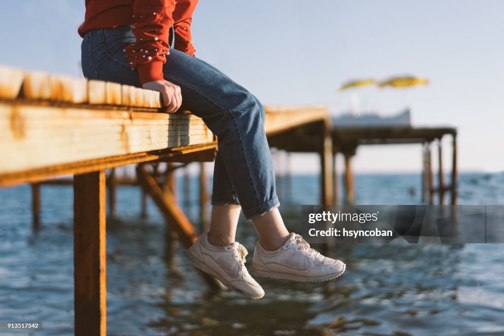 Woman's feet dangle from wooden wharf, above sea