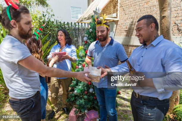 group of mixed race people giving gifts at a christmas party - sydney christmas lights 2017 stock pictures, royalty-free photos & images