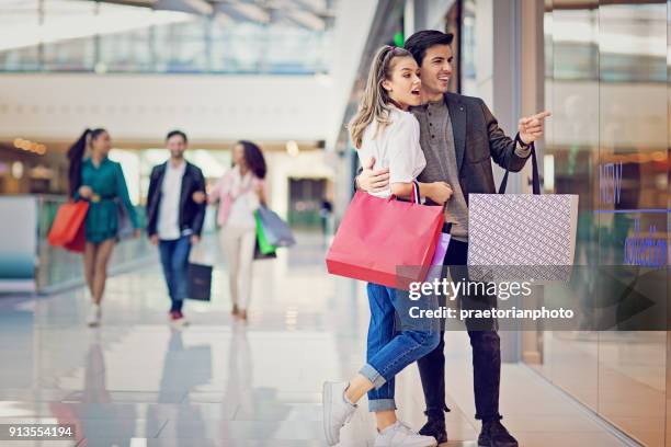 shopping couple is looking in the store window in the mall - couple shopping in shopping mall stock pictures, royalty-free photos & images