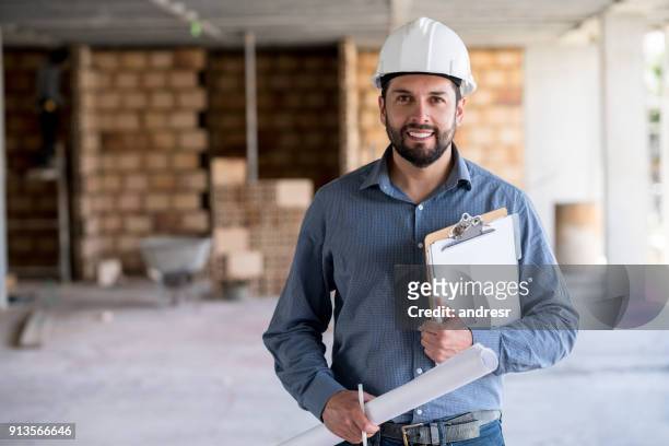 portrait of an engineer holding a blueprint at a construction site - architect stock pictures, royalty-free photos & images