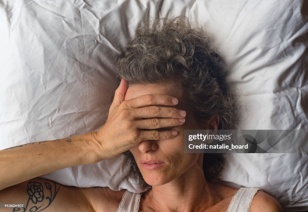 Middle aged woman with hand over eyes on pillow from abvove