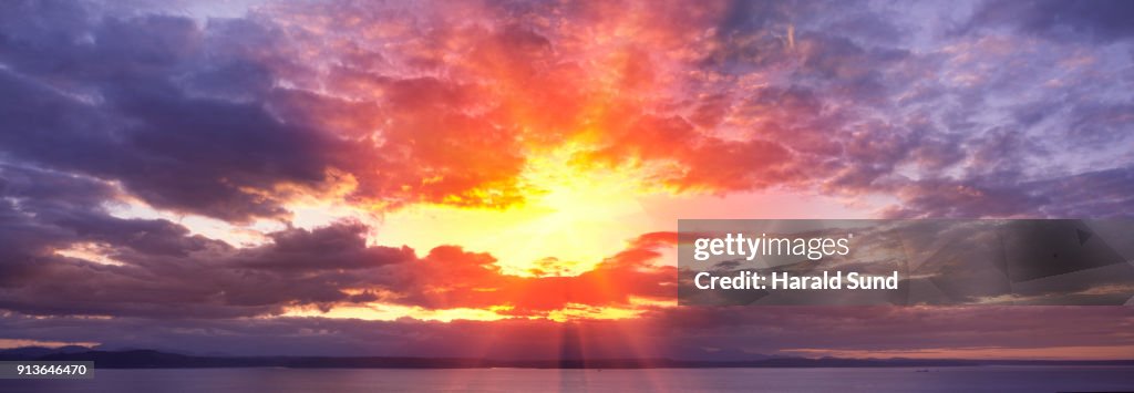 Panorama of a setting sun and surrounding clouds over the waters of Puget Sound.