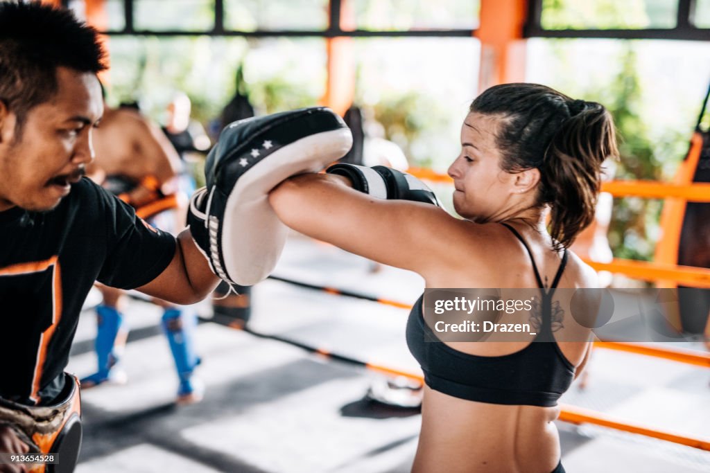 Teamwork with personal trainer in Muay Thai camp in Thailand - young woman using elbow punch