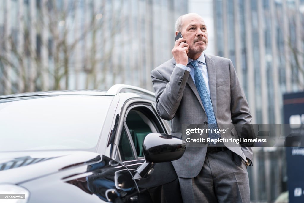 Ein Geschäftsmann lehnt sich an ein Auto und führt ein Telefonat