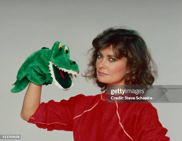 Portrait of American actress Jane Badler as she poses with an alligator hand puppet, Los Angeles, California, 1984.