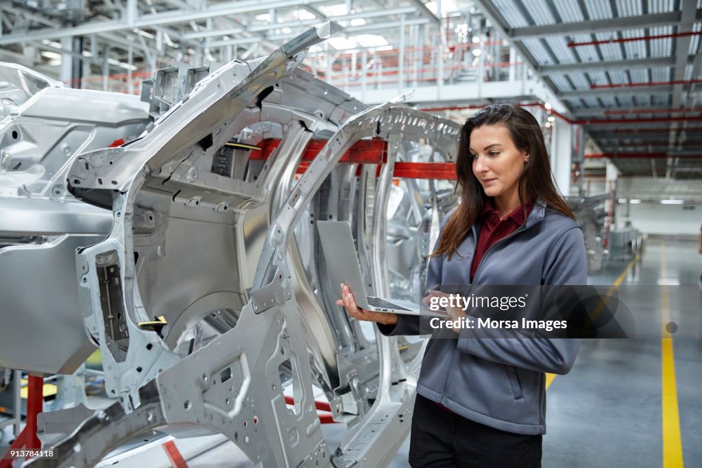 Maintenance engineer using laptop by car chassis
