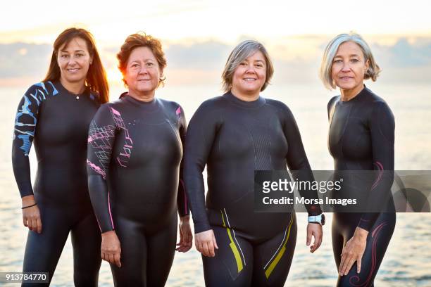 Female friends in wetsuits smiling at beach