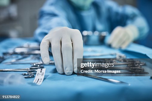 Surgeon picking up surgical tool from tray Surgeon picking up surgical tool from tray
