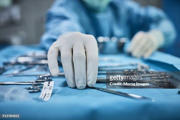 surgeon picking up surgical tool from tray - surgical glove stock pictures, royalty-free photos & images