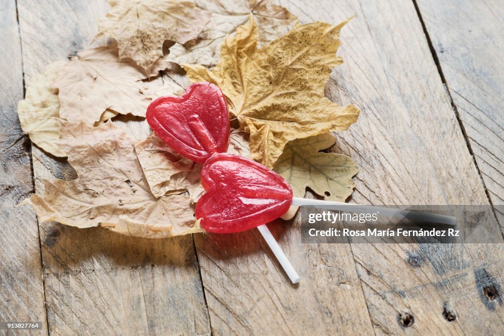 Dry leaves and two heart shape lollipops on old wooden background. Selective focus and copy space.