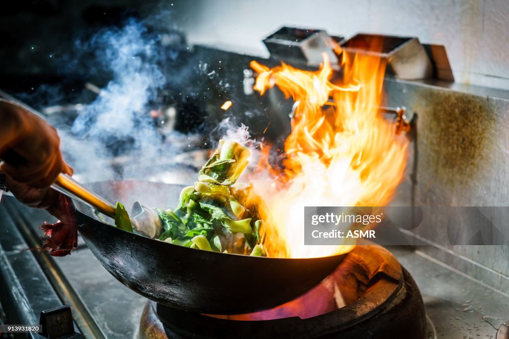 Chef in restaurant kitchen at stove with high burning flames