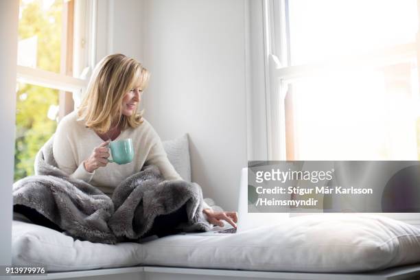 vrouw gewikkeld in een deken met behulp van laptop thuis - middle aged woman winter stockfoto's en -beelden