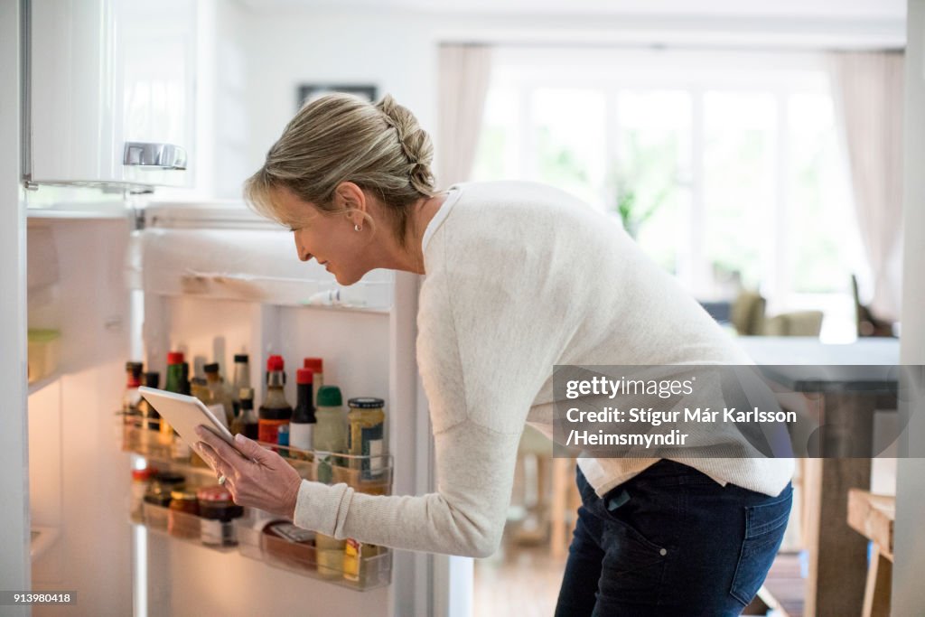 Donna con tablet PC che guarda in frigorifero