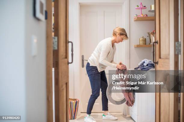 mature woman loading clothes in washing machine - afazeres domésticos imagens e fotografias de stock