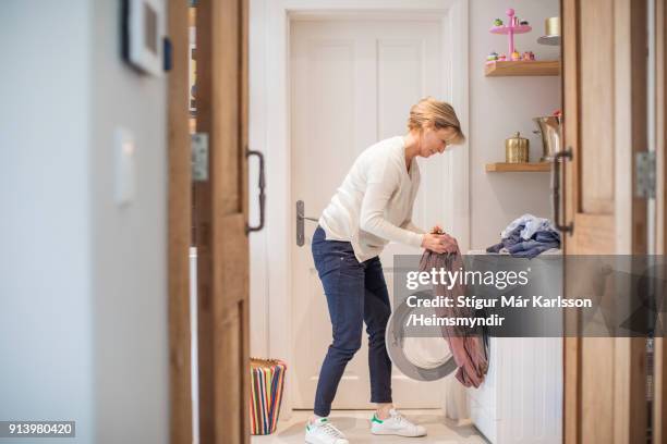 mature woman loading clothes in washing machine - máquina de lavar roupa imagens e fotografias de stock