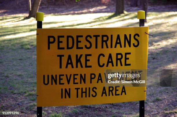 sign warning pedestrians to take care because of uneven pavement in this area - trip hazard stock pictures, royalty-free photos & images