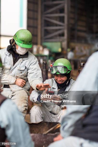 two guys looking and laughing at a smart phone in a shipbuilding factory - scheepsbouwer stockfoto's en -beelden