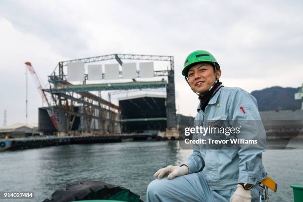 a worker on a boat in front of a large shipbuilding factory - coveralls stock pictures, royalty-free photos & images