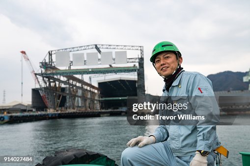 A worker on a boat in front of a large shipbuilding factory A worker on a boat in front of a large shipbuilding factory