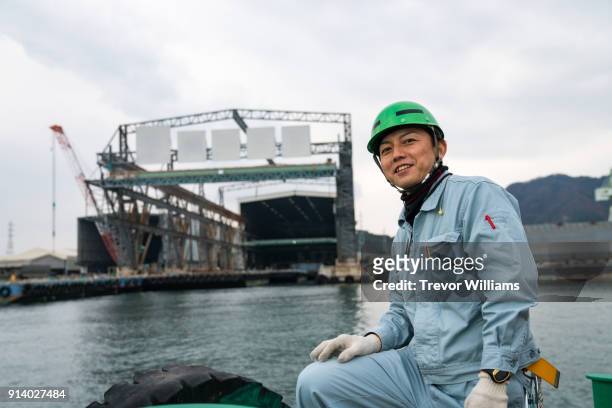 a worker on a boat in front of a large shipbuilding factory - 連身工作服 個照片及圖片檔