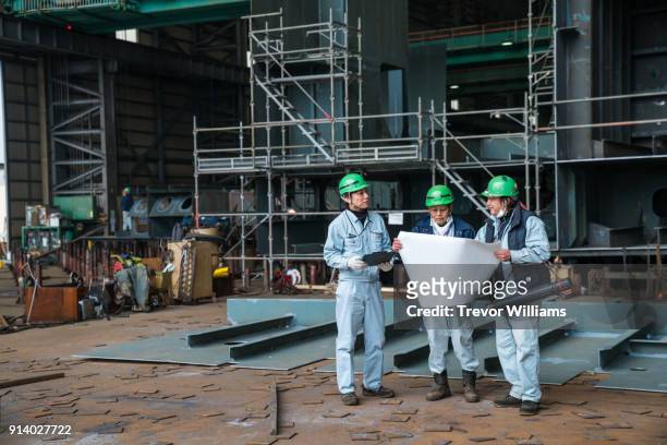 three people discussing blueprints or building plans in a shipbuilding factory - senior blaumann stock-fotos und bilder
