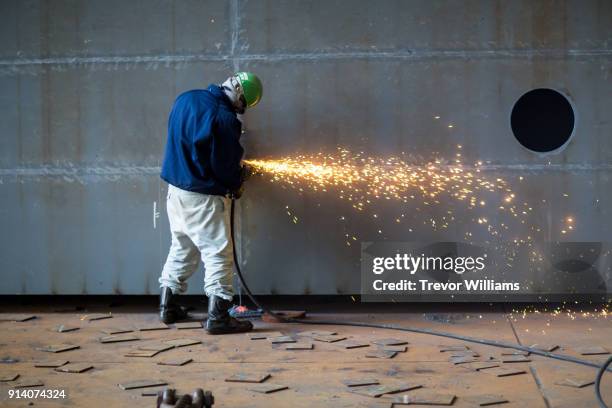 a man grinding steel at a large shipbuilding factory - shipbuilder stock pictures, royalty-free photos & images