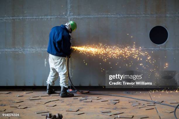 a man grinding steel at a large shipbuilding factory - construtor de navios imagens e fotografias de stock