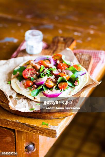 homemade wheat flat bread with fresh chard leaves, roasted cherry tomatoes, red onion and crispy bacon with cream cheese sauce on a wooden cutting board for a snack for picnic, selective focus - indoor picnic stock pictures, royalty-free photos & images