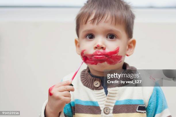 sweet little toddler boy covering his face with red lipstick - boy funny face ストックフォトと画像