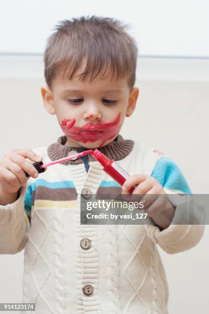 sweet little toddler boy covering his face with red lipstick - red lipstick smudge stock pictures, royalty-free photos & images