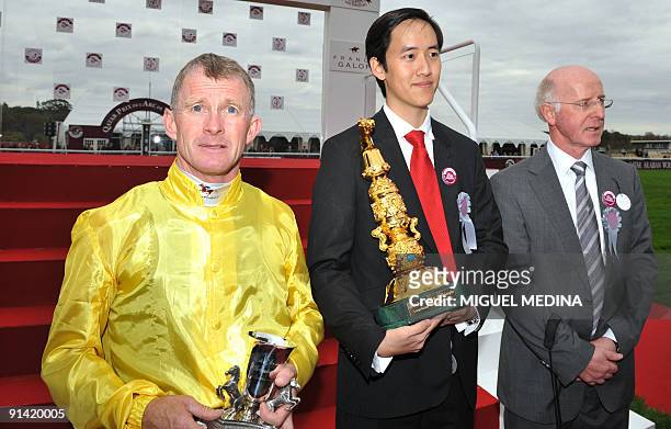 Irish jockey Mickael Kinane poses on the podium next to the racehorse owner Christopher Tsui and his coach John Oxx after winning with "Sea the...