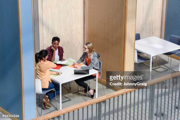 tres alumnas discutiendo alrededor de mesa en cabina, de vista elevado - confidential palabra en inglés fotografías e imágenes de stock