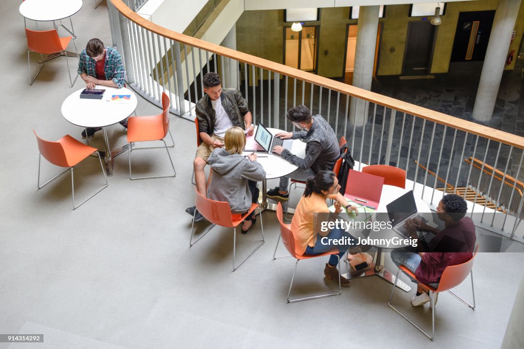 Studenten sitzen an Tischen mit Laptops und Treffen mit Freunden