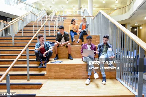 college friends sitting on steps in modern interior, chatting and using laptop - sitting indoor stock pictures, royalty-free photos & images