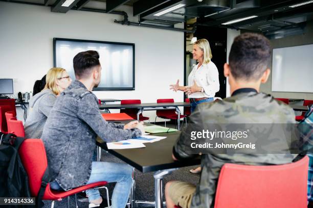 college lecturer talking to young students in modern classroom - small group of people stock pictures, royalty-free photos & images