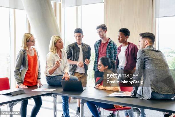 six college students listening to mature female lecturer with laptop in classroom - showing stock pictures, royalty-free photos & images