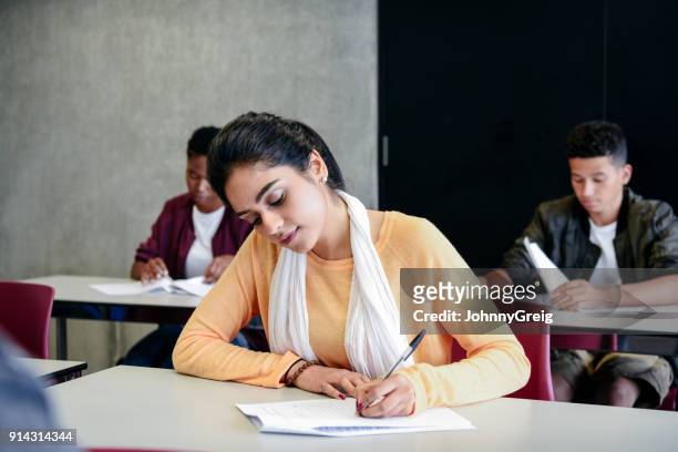 young woman taking an exam writing at desk in classroom - writing stock pictures, royalty-free photos & images