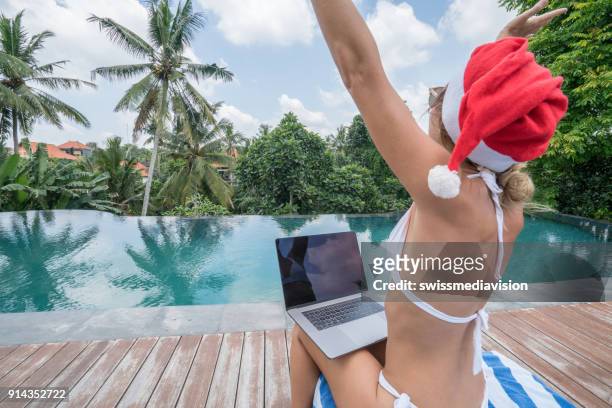 kerst vakanties in tropisch klimaat vrouw met laptop bij zwembad, uitgestrekte armen - infinity pool stockfoto's en -beelden
