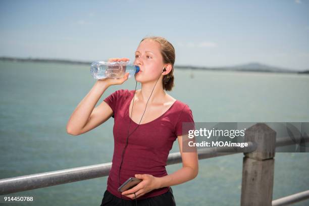 a young caucasian girl is drinking by the sea after exercise - rangitoto stock pictures, royalty-free photos & images