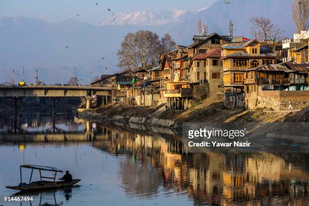 Boatman crosses river Jehlum as the buildings are reflected on the river during a sunny day in warm winter on February 5, 2018 in Srinagar, the...