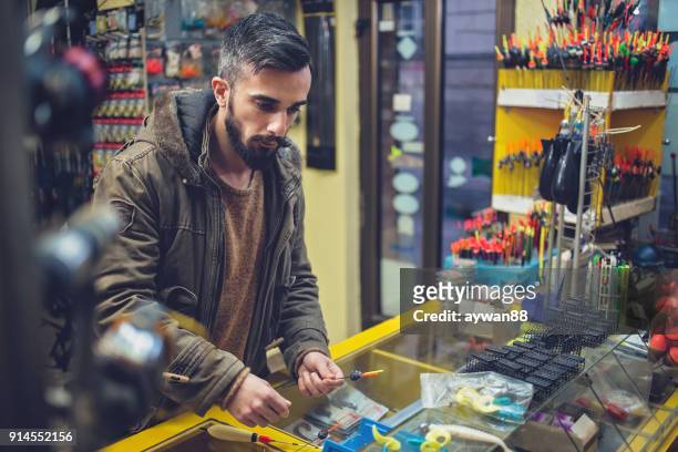 young man buying new fishing equipment - barbed hook stock pictures, royalty-free photos & images