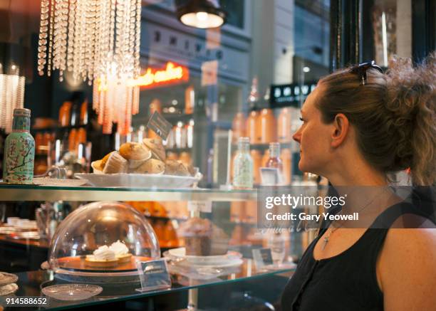 portrait of a woman looking into a cake shop window - bakery window stock pictures, royalty-free photos & images