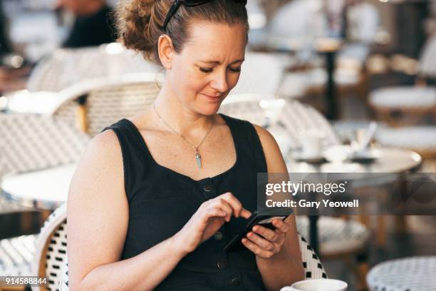 portrait of a woman with phone at a cafe table in bordeaux - mouwloos stockfoto's en -beelden